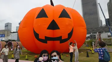 Seorang wanita mengenakan masker untuk mencegah penyebaran virus corona, berpose untuk selfie di depan dekorasi buah labu besar untuk Halloween di sebuah taman di Hong Kong, Rabu (27/10/2021). Tahun ini, perayaan tersebut jatuh pada hari Minggu, 31 Oktober 2021. (AP Photo/Vincent Yu)