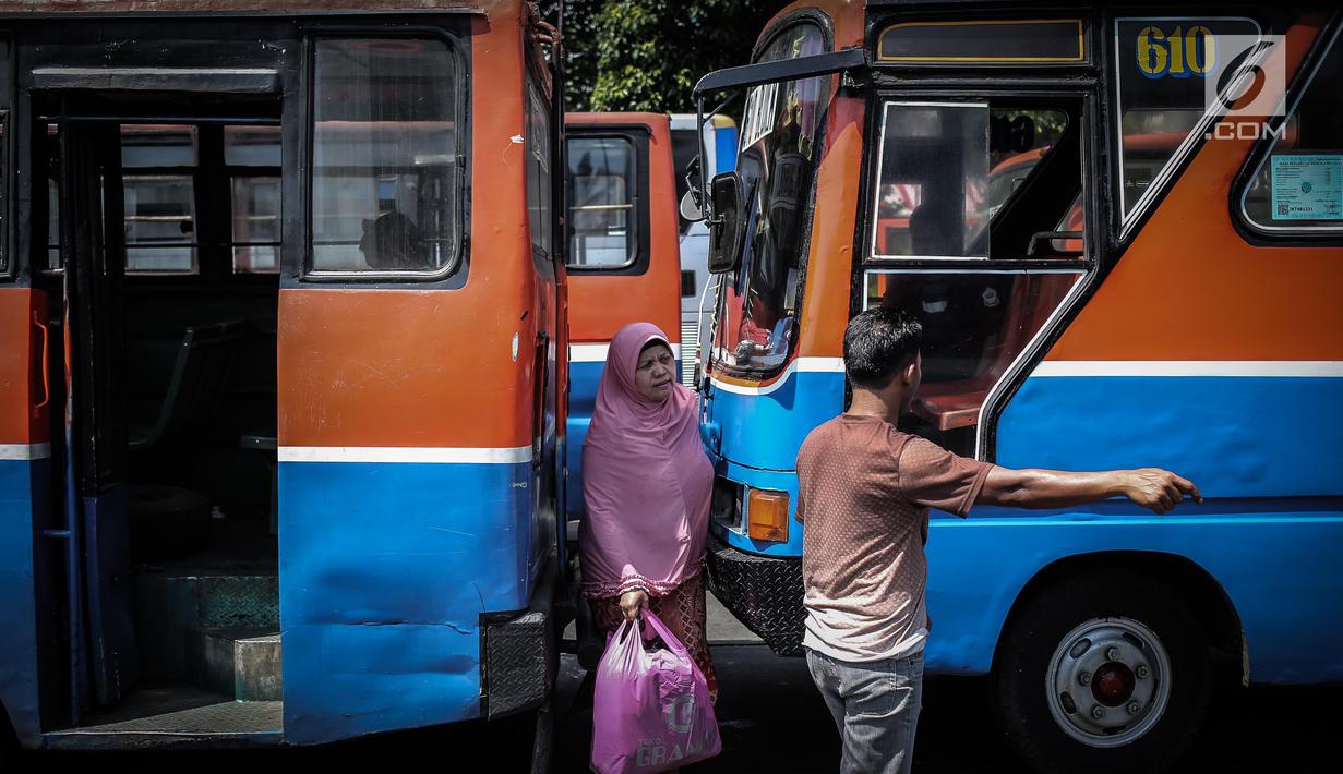 Seorang wanita melintas diantara Metromini di Terminal Blok M, Jakarta, Rabu (26/7). Menurut pihak Dishub DKI, revitalisasi tersebut melibatkan langsung para pemilik kendaraan Metromini. (Liputan6.com/Faizal Fanani)