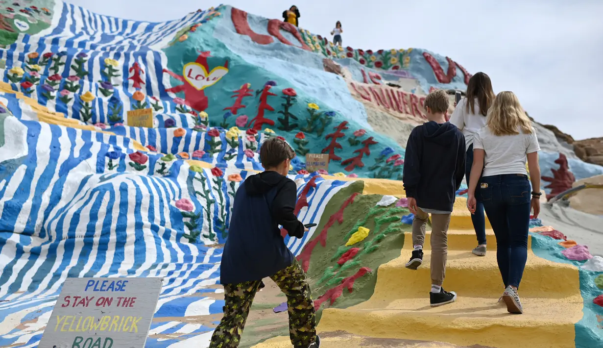 Turis mengunjungi Salvation Mountain, sebuah lereng bukti di Niland, California, Amerika Serikat. Salvation Mountain memiliki lebar 46 meter, dan panjang 15,2 meter ini tidak dihiasi pepohonan, melainkan tulisan dan gambar warna-warni dengan pesan cinta. (Robyn Beck/AFP)