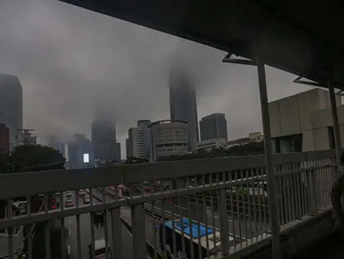 Warga melintas di salah satu Jembatan Penyeberangan Orang (JPO) berlatar suasana gedung bertingkat yang diselimuti kabut di sekitar jalan Jenderal Gatot Subroto, Jakarta, Sabtu (6/7/2024). (Liputan6.com/Angga Yuniar)