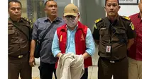 Tersangka korupsi Ujang Iskandar, dengan tangan terborgol dan wajah tertutup topi serta masker, tiba di Palangka Raya diiringi oleh petugas kejaksaan, Rabu (21/8/2024).