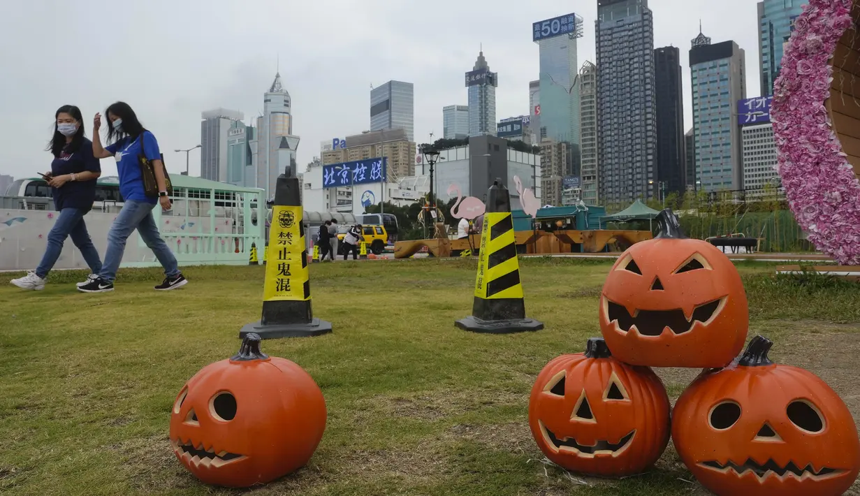 Orang-orang yang memakai masker untuk mencegah penyebaran virus corona, berjalan melewati dekorasi Halloween di sebuah taman di Hong Kong, Rabu (27/10/2021). (AP Photo/Vincent Yu)