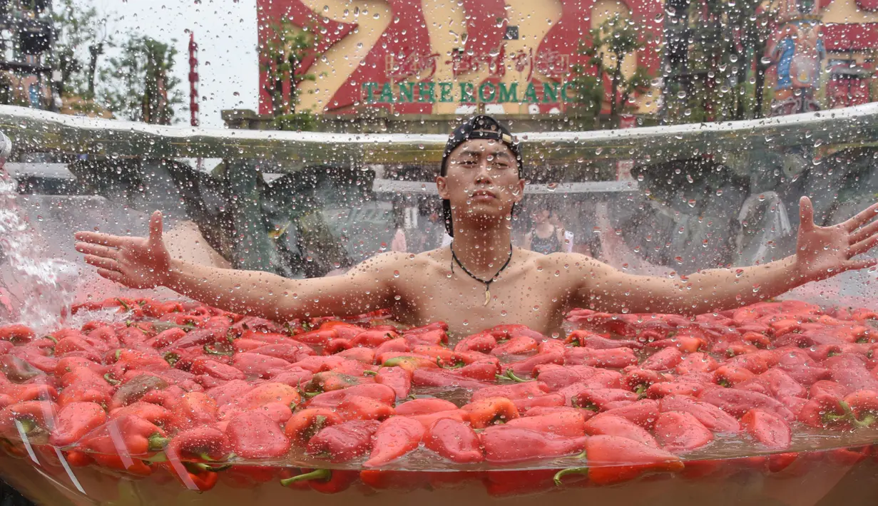 Seorang peserta berendam dalam gentong berisi cabai yang direndam air selama kompetisi makan cabai di Ningxiang, Provinsi Hunan, Tiongkok, 12 Agustus 2017. Kompetisi ini berhasil dimenangkan oleh seorang peserta yang mampu memakan 15 cabai. (STR / AFP)