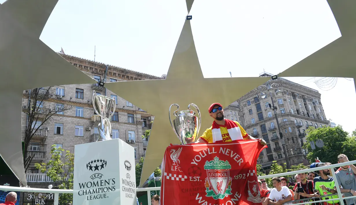 Fans Liverpool berpose di samping piala Liga Champions yang dipamerkan di Kiev, Ukraina , Kamis (24/5). Pertandingan final antara Liverpool dan Real Madrid akan berlangsung di Olimpiyskiy Stadium. (Sergei SUPINSKY/AFP)