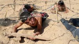 Seorang anak Palestina merangkak di bawah kawat berduri selama latihan militer di sebuah kamp musim panas yang diselenggarakan oleh Islamic Jihad Movement di Khan Younis di Jalur Gaza selatan (13/7). (REUTERS/Ibraheem Abu Mustafa)