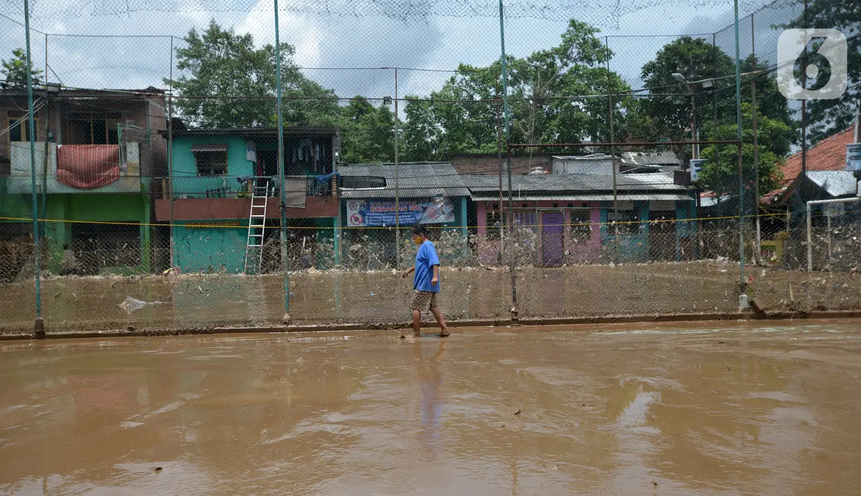 Warga berjalan melewati lumpur sisa banjir di Kelurahan Rawa Jati, Jakarta, Selasa (9/2/2021). Endapan lumpur yang mengendap akibat luapan Kali Ciliwung. (merdeka.com/Imam Buhori)