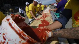 Sejumlah peserta menaburi saus tomat saat membuat pizza panjang di jalur Auto Club Speedway, di Fontana, California (10/6). Rekor baru ini mengalahkan rekor sebelumnya yang dipegang oleh peserta di Italia dengan pizza sepanjang 1,8 km. (AFP/Mark Ralston)