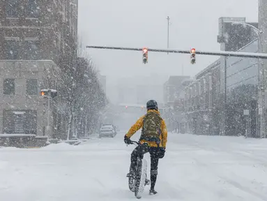 Seorang pria di sepedanya menunggu lampu merah selama badai salju di pusat kota Kalamazoo, Michigan, Rabu (2/2/2022). Badai musim dingin besar dengan jutaan orang Amerika di jalurnya membawa campuran hujan dan salju ke bagian tengah Amerika Serikat. (Joel Bissell/Kalamazoo Gazette via AP)