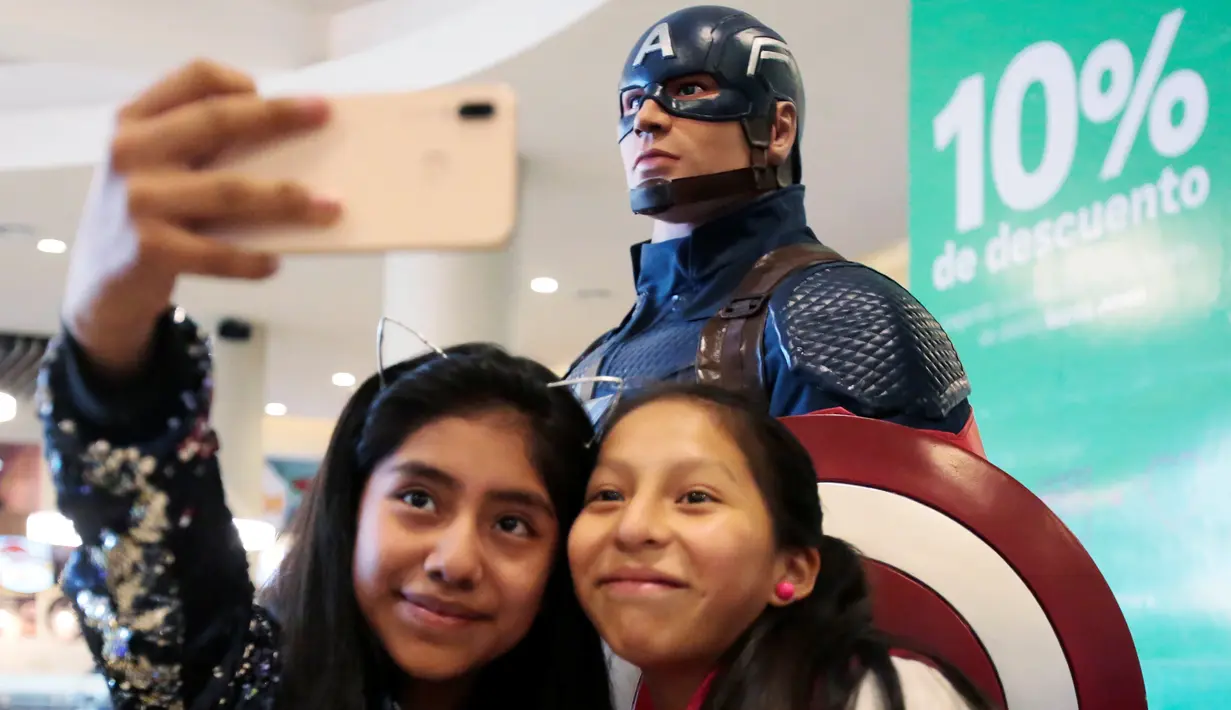 Dua penggemar wanita berselfie di dekat patung Captain America saat mengantre untuk menyaksikan pemutaran perdana film The Avengers: Endgame di La Paz, Bolivia (24/4). Film Avengers ini diputar perdana secara serentak pada 24 April 2019. (Reuters/David Mercado)