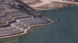 Garis air terlihat di tepi curam Danau Oroville saat seorang nelayan mengapung di Oroville, California (1/6/2021). Volume air waduk Danau Oroville yang terus menyusut saat ini menyisakan kapasitas 38 persen. (AFP/Justin Sullivan)