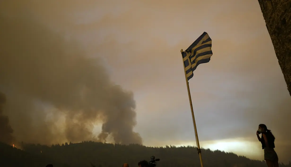 Seorang penduduk setempat berdiri di atas bukit saat api mendekat di desa Gouves di pulau Evia, sekitar 185 kilometer (115 mil) utara Athena, Yunani, Minggu (8/8/2021). Kebakaran hutan yang berlangsung selama beberapa hari melahap hutan dan merambah ke desa-desa. (AP Photo/Petros Karadjias)