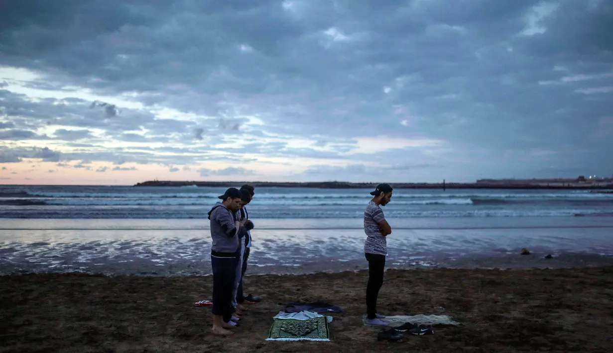 Sejumlah pria salat Maghrib berjamaah usai buka puasa bersama di pantai Rabat, Maroko (9/6). Selama Ramadan, banyak warga Maroko berkunjung ke pantai menikmati angin Atlantik dan menikmati pemandangan laut. (AP Photo/Mosa'ab Elshamy)