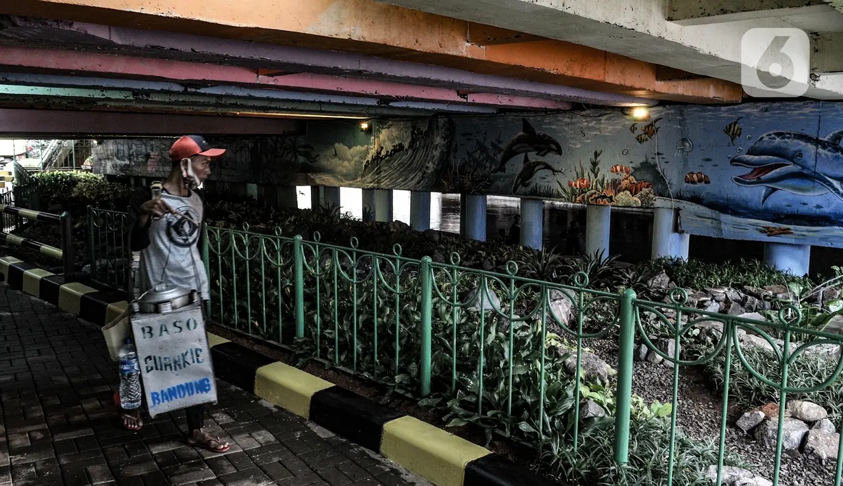 Pedagang melintasi taman kolong Jembatan Pegangsaan, Jakarta, Minggu (7/2/2021). Penataan taman di kolong Jembatan Pegangsaan rampung dibangun yang kini telah dilengkapi tanaman hias, kolam ikan, mural, lampu warna-warni dan area untuk interaksi warga. (merdeka.com/Iqbal S Nugroho)