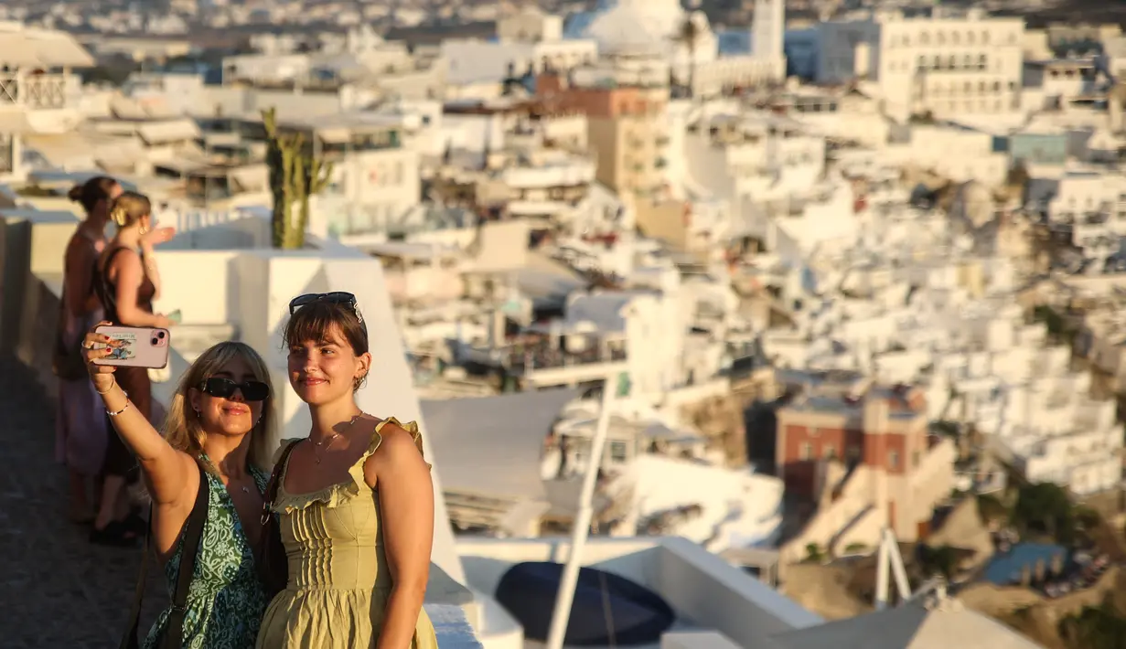 Saat matahari terbenam di balik cakrawala di Oia, ribuan orang mengangkat ponsel mereka ke langit untuk mengabadikan momen tersebut, diikuti dengan tepuk tangan meriah. (Aris Oikonomou / AFP)