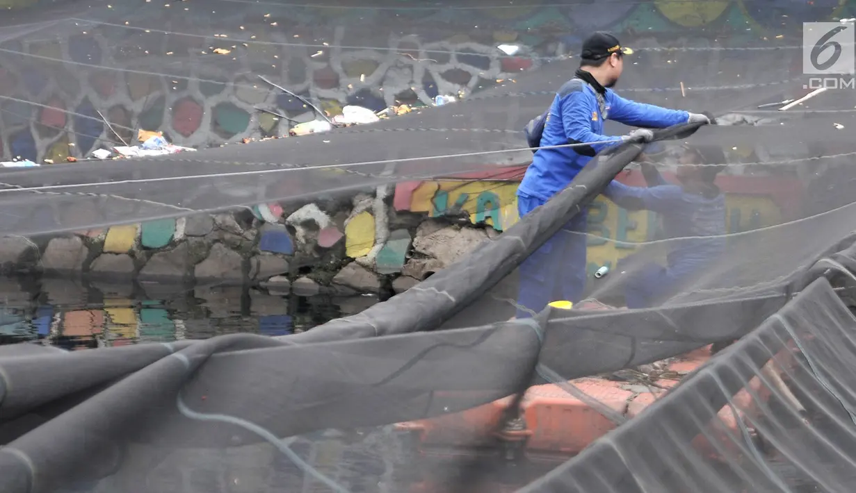 Petugas melepas kain waring atau jaring yang menutupi Kali Item di Kemayoran Jakarta, Rabu (14/11). Pelepasan waring yang sebagian dalam kondisi sudah robek itu dilakukan lantaran banyak warga yang membuang sampah di atasnya (Merdeka.com/Iqbal S. Nugroho)