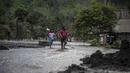 Warga melintasi air yang mengalir melewati rumah-rumah yang rusak di Dusun Kamar Kajang, Lumajang, Kamis (9/12/2021). Luapan air sungai bercampur material lahar dingin erupsi Gunung Semeru merendam puluhan rumah akibat diguyur hujan deras pada Selasa (7/12) dan Rabu (8/12) malam (Juni Kriswanto/AFP)