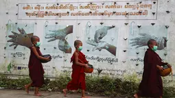 Biksu pemula Buddha yang mengenakan masker berjalan melewati papan peringatan COVID-19 saat mereka mengumpulkan sedekah pagi di Yangon, Myanmar, Kamis (15/7/2021). Myanmar mencatat rekor kematian harian karena virus corona yaitu 80 kasus dan 5.014 kasus infeksi baru. (AP Photo/Thein Zaw)