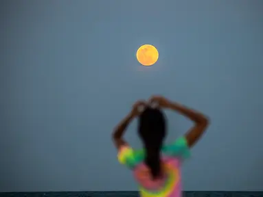 Bulan Purnama Super Pink terlihat di latar belakang saat orang-orang bersantai di pantai di Miami Beach, Florida, Senin (26/4/2021). Super Pink Moon merupakan fenomena alam ketika posisi bulan purnama berada terdekat dengan bumi. (CHANDAN KHANNA / AFP)