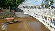 Perahu melintas di bawah Pembangunan jembatan penyeberangan orang (JPO) sungai Ciliwung, Jakarta, Senin (4/4). Rencaanya JPO tersebut siap digunakan pada 6 April mendatang. (Liputan6.com/Yoppy Renato)