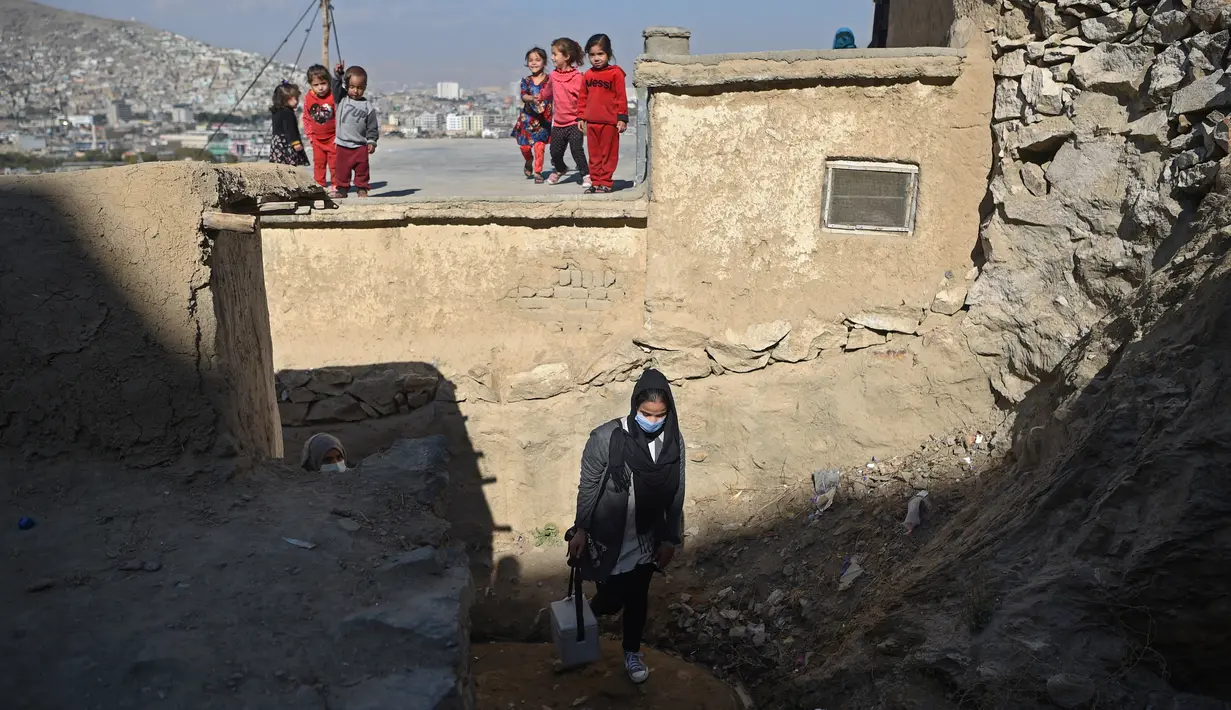 Seorang petugas kesehatan berjalan ketika anak-anak melihatnya selama kampanye vaksinasi di Kabul, Afghanistan pada 8 November 2021. Vaksinasi tersebut merupakan yang pertama sejak Taliban berkuasa di Afghanistan. (WAKIL KOHSAR / AFP)