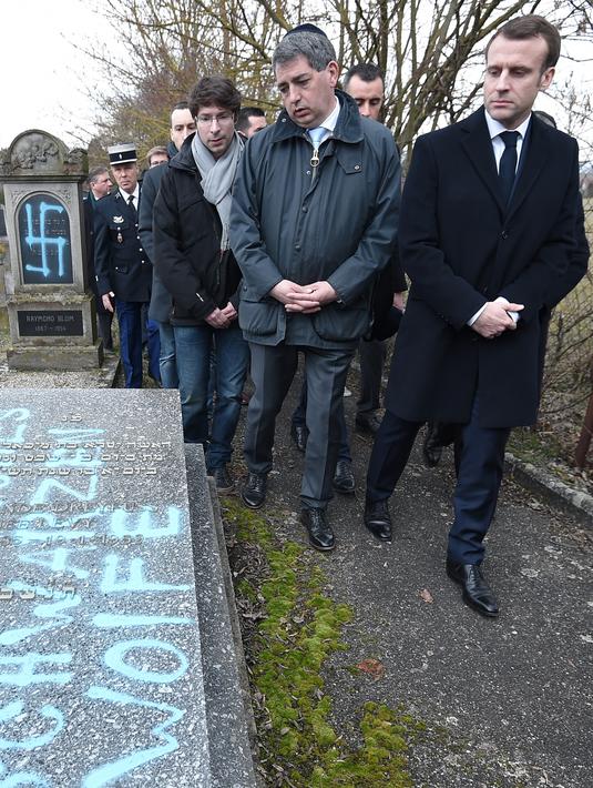 Presiden Prancis Emmanuel Macron melihat makam Yahudi yang dicoret simbol Nazi di pemakaman Yahudi, Quatzenheim, Prancis, Selasa (19/2). Macron menyatakan pelaku tidak layak menjadi warga Prancis. (Frederick FLORIN/AFP)