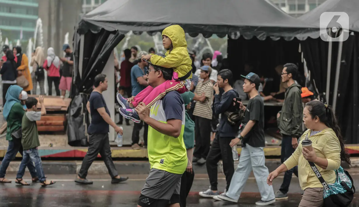 Warga menggendong anak kecil saat car free day (CFD) di kawasan Bundaran HI, Jakarta, Minggu (29/12/2019). Kendati tidak seramai saat cerah, warga yang berlari, jalan santai, atau swafoto masih menjadi pemandangan di area CFD usai hujan mengguyur Jakarta. (Liputan6.com/Faizal Fanani)