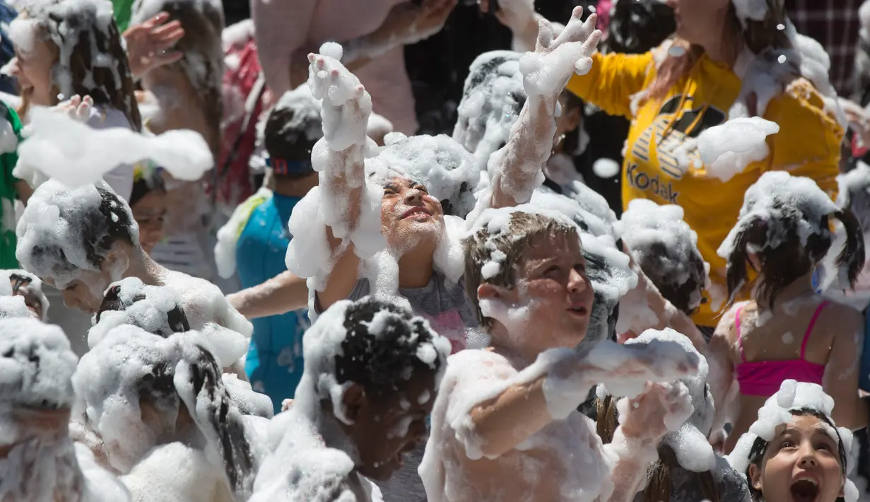Orang tua dan anak-anak disemprot dengan busa oleh petugas pemadam kebakaran selama pesta di distrik Malasana Madrid, Spanyol, (4/5/2019). (AP Photo/Paul White)