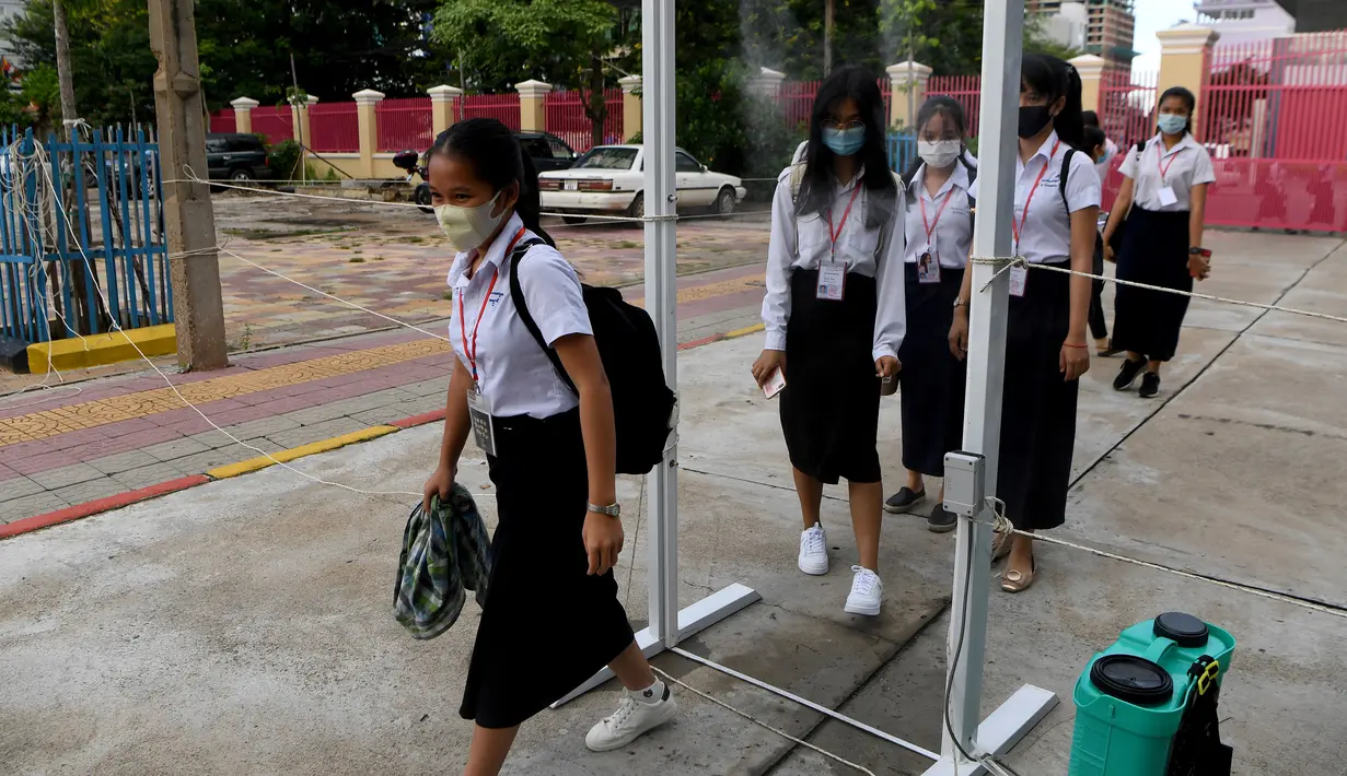 Para siswa yang mengenakan masker berjalan melalui gerbang yang dilengkapi dengan semprotan desinfektan ketika sekolah dibuka kembali di Phnom Penh, Senin (7/9/2020). Sekolah-sekolah di Kamboja dibuka kembali pada Senin (7/9) setelah enam bulan ditutup akibat COVID-19. (TANG CHHIN Sothy /AFP)