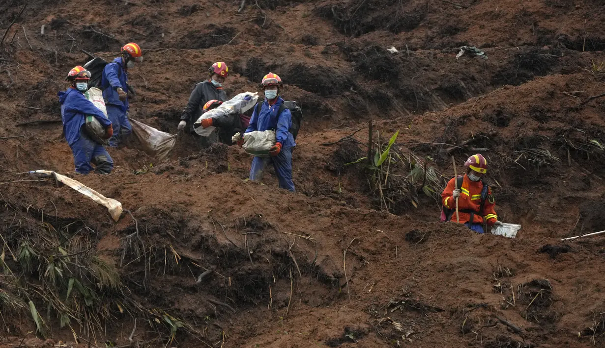 Pekerja darurat yang membawa barang-barang yang dibungkus tas turun dari lereng bukit setelah melakukan operasi pencarian di dekat lokasi kecelakaan pesawat Boeing 737-800 milik China Eastern Airlines di desa Molang, di provinsi Guangxi, China barat daya, Rabu (24/3/2022). (AP Photo/Ng Han Guan)