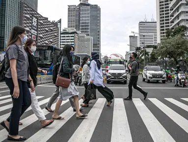 Orang-orang menyeberang jalan dengan latar belakang gedung perkantoran di kawasan Sudirman, Jakarta, Rabu (16/12/2020). Pemprov DKI Jakarta akan mengikuti arahan Wakil Ketua Komite Penanganan Covid-19 Luhut Binsar Pandjaitan terkait pengetatan work from home (WFH). (Liputan6.com/Faizal Fanani)