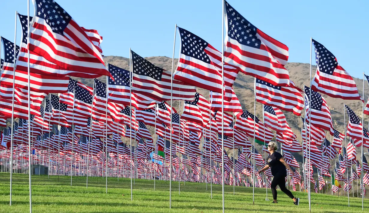 Seorang wanita berjalan melewati pameran bendera AS untuk peringatan 20 tahun serangan 9/11 di Pepperdine University di Malibu, Rabu (8/9/2021). Selama 14 tahun, universitas itu memperingati tragedi 11 September 2001 dengan mengibarkan sekitar 3.000 bendera Amerika. (Frederic J. BROWN/AFP)
