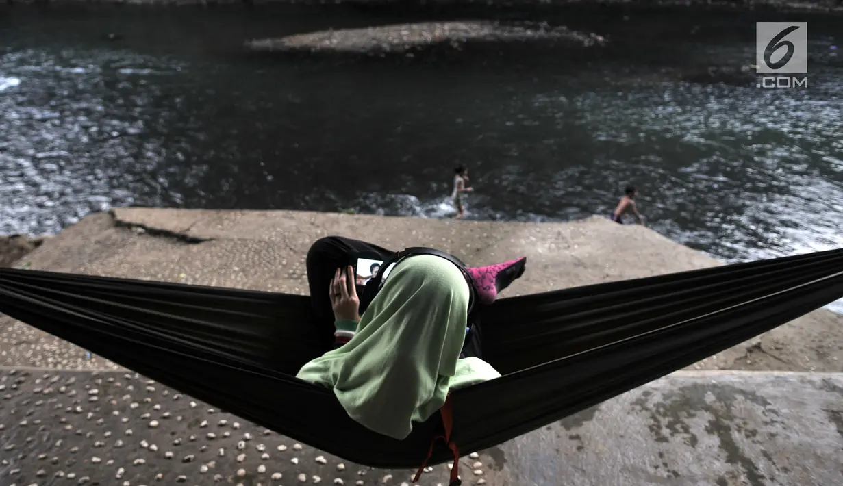 Warga bersantai di pinggir aliran Sungai Ciliwung, Depok, Jawa Barat, Kamis (4/7/2019). Menurunnya debit air Sungai Ciliwung akibat musim kemarau dimanfaatkan warga setempat sebagai tempat wisata gratis untuk mengajak anak berenang. (merdeka.com/Iqbal Nugroho