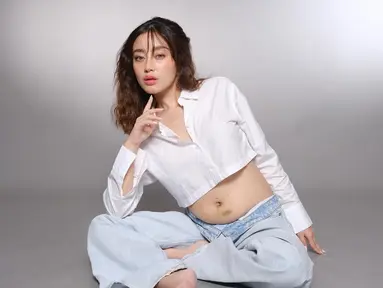 Tasya tampil menawan dengan balutan kemeja putih crop top dan celana jeans longgar. Dengan pose santai di lantai, ia memancarkan kebahagiaan dan kebanggaan atas kehamilan keduanya. Senyumnya yang lembut semakin menambah aura kehangatan dalam foto tersebut. (Liputan6.com/IG/@tasyarevina)