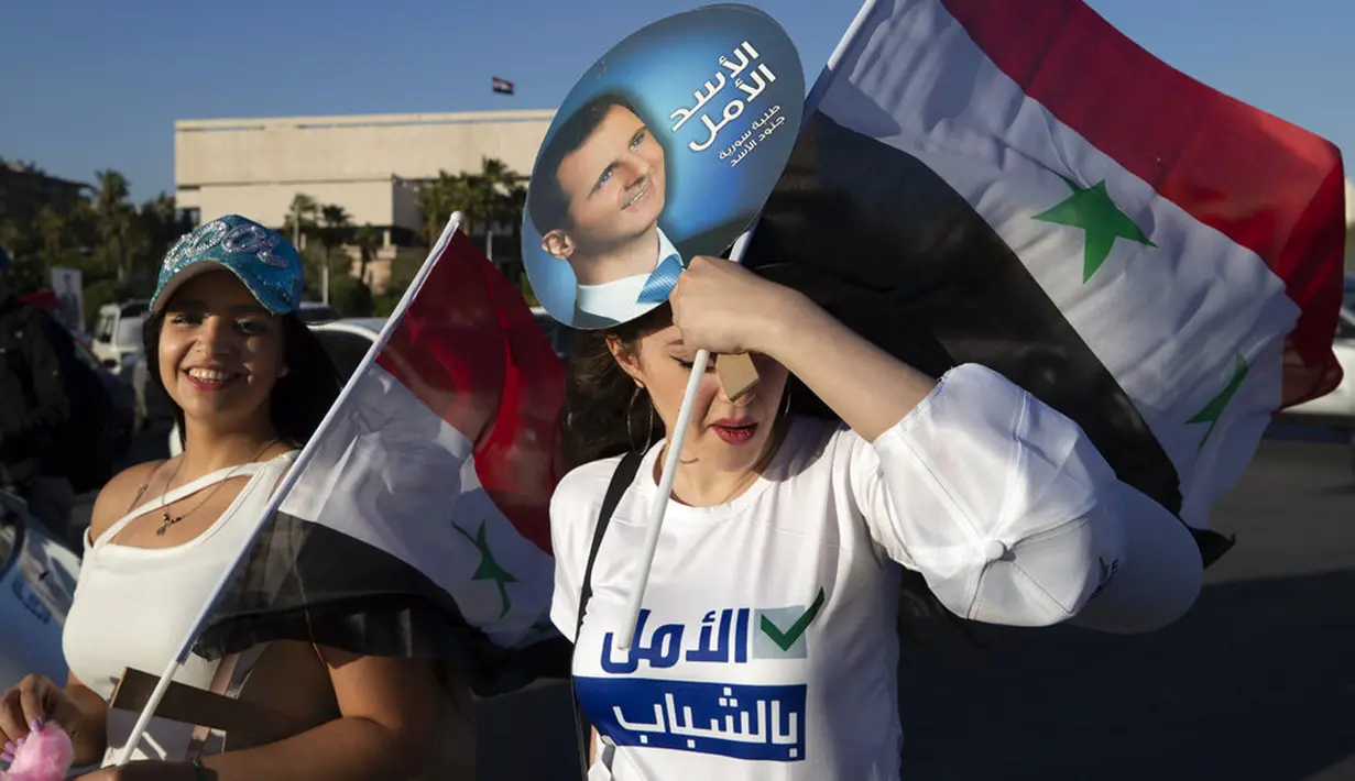 Pendukung Presiden Suriah Bashar Assad berpose untuk berfoto saat mereka memegang bendera Suriah dan foto Assad pada pertemuan di Omayyid Square, Damaskus, Suriah, Minggu (23/5/2021). Pemilihan presiden di negara yang dilanda perang itu akan diadakan pada 26 Mei. (AP Photo/Hassan Ammar)
