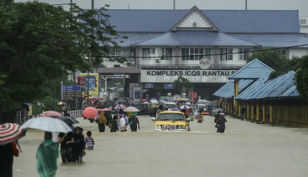 Warga menerobos banjir yang menggenangi jalanan di depan Kantor imigrasi dan bea cukai di Rantau Panjang, Selasa (3/1). Akibat hujan lebat yang turun terus menerus selama empat hari di Malaysia, 5000 warga terpaksa dievakuasi. (AFP PHOTO/STR/Malaysia OUT)