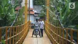 Pengendara motor melintasi jembatan gantung Kuning yang menghubungkan Pasar Minggu Poltangan ke Cililitan Condet, Jakarta, Selasa (28/12/2021). Jembatan gantung Kuning tersebut merupakan jalan umum dan akses jalan warga yang ingin berlalu-lalang. (merdeka.com/Imam Buhori)
