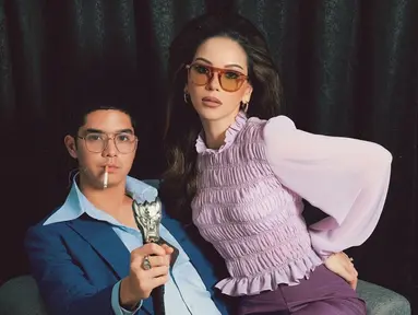 Dalam foto ini, Al Ghazali duduk di kursi dengan mengenakan setelan jas biru tua yang khas, lengkap dengan kemeja berkerah lebar yang terbuka. Dengan tatapan tajam, ia memegang tongkat yang mirip dengan gaya Elvis Presley, menambah kesan berani dan karismatik. Di sampingnya, Alyssa Daguise tampil anggun dalam balutan atasan ungu muda yang bertekstur, mengingatkan kita pada gaya Priscilla yang ikonik. (Liputan6.com/IG/@alyssadaguise)