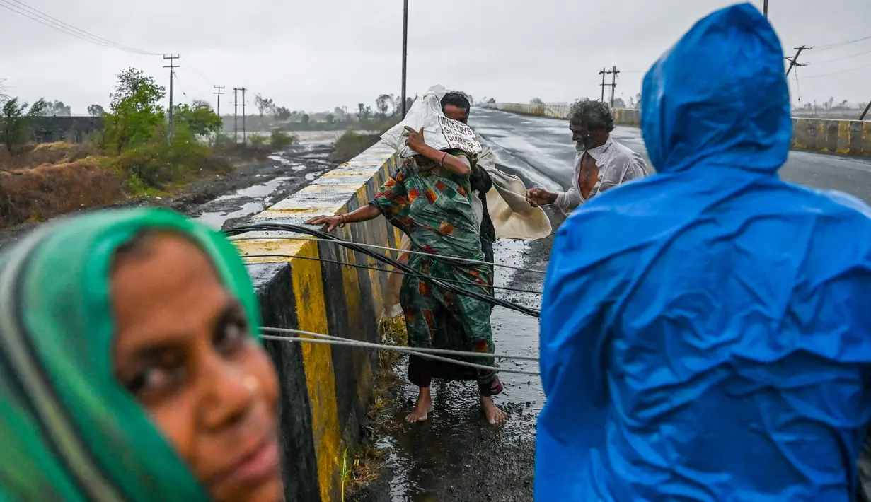 Penduduk desa mencoba untuk menyeberangi kabel listrik yang jatuh di jembatan dekat Diu setelah siklon Tauktae menghantam pantai barat India pada Selasa (18/5/2021). Topan Tauktae disebut yang terbesar melanda wilayah itu dalam beberapa dekade terakhir. (Punit PARANJPE / AFP)