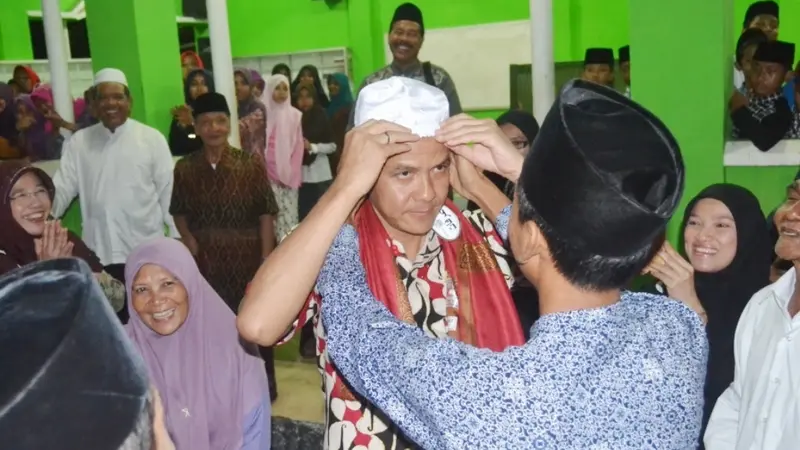 Seorang santri memakaikan peci atau kopyah kepada Ganjar Pranowo saat kunjungan ke pesantren El Bayan, Majenang, Cilacap. (Liputan6.com/Muhamad Ridlo)