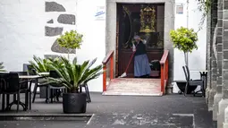Biarawati membersihkan pintu masuk gereja yang tertutup abu dari gunung berapi di Pulau Canary La Palma, di Los Llanos de Aridane, Spanyol (1/10/2021). Retakan baru ini adalah yang ketiga yang retak terbuka sejak kawah Cumbre Vieja meletus di pulau La Palma 19 September. (AP Photo/Saul Santos)