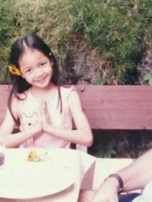 Pertama adalah foto masa kecil Lisa, dengan bunga berwarna kuning yang diselipkan ke telinga, Lisa kecil tersenyum manis ke kamera sembari menangkupkan tangannya di depan dada. (Foto: Instagram/ roses_are_rosie)