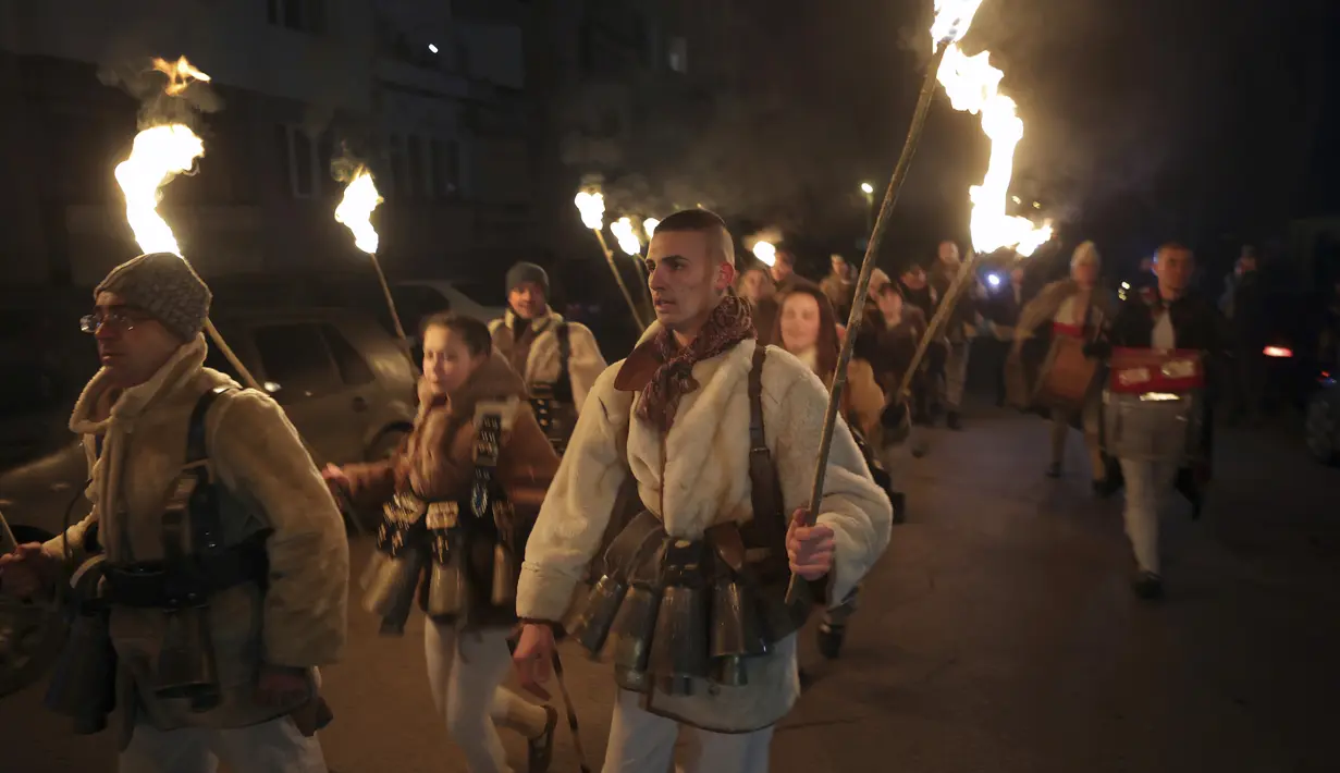 Penari membawa obor saat ritual kuno mengusir roh jahat di jalan-jalan Batanovci, Bulgaria, Kamis malam (13/1/2022). Setiap musim dingin di desa-desa seluruh negara Balkan, pria, wanita dan anak-anak mengenakan topeng ritual dan kostum melakukan tarian di sekitar api unggun. (AP/Valentina Petrova)