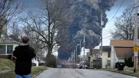 Seorang pria mengambil foto saat gumpalan hitam membumbung tinggi di Palestina Timur, Ohio, akibat ledakan terkendali sebagian kereta Norfolk Southern yang tergelincir, 6 Februari 2023. (Dok: Gene J. Puskar / The Associated Press)