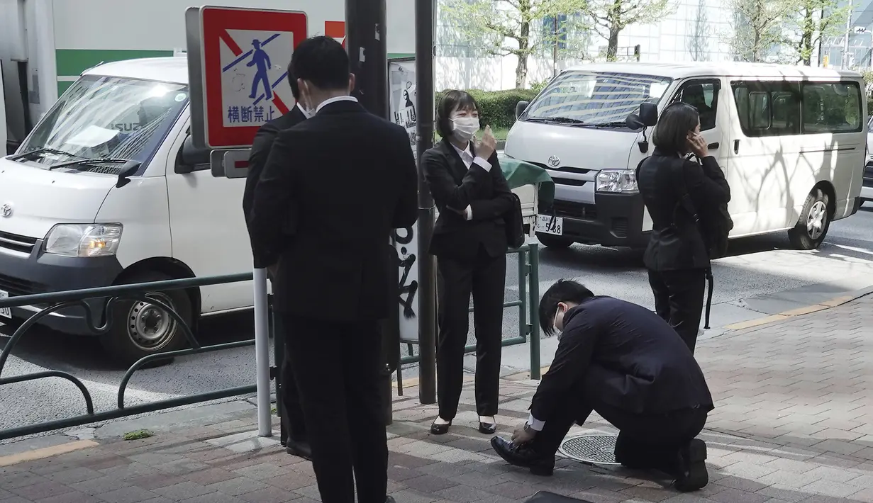 Karyawan yang mengenakan masker pelindung untuk membantu mengekang penyebaran virus corona COVID-19 berdiri di trotoar Tokyo, Jepang, Rabu (7/4/2021). Tokyo mengonfirmasi lebih dari 550 kasus COVID-19 baru pada 7 April 2021. (AP Photo/Eugene Hoshiko)