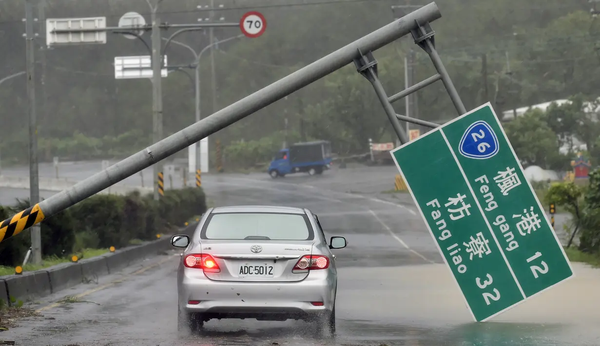 Mobil melewati papan penunjuk jalan yang ambruk akibat hantaman topan super Meranti di  Taiwan selatan, Rabu (14/9). Sejumlah kerusakan, seperti tiang listrik roboh dan banyaknya pohon tumbang dilaporkan terjadi akibat terjangan topan itu. (Sam YEH/AFP)