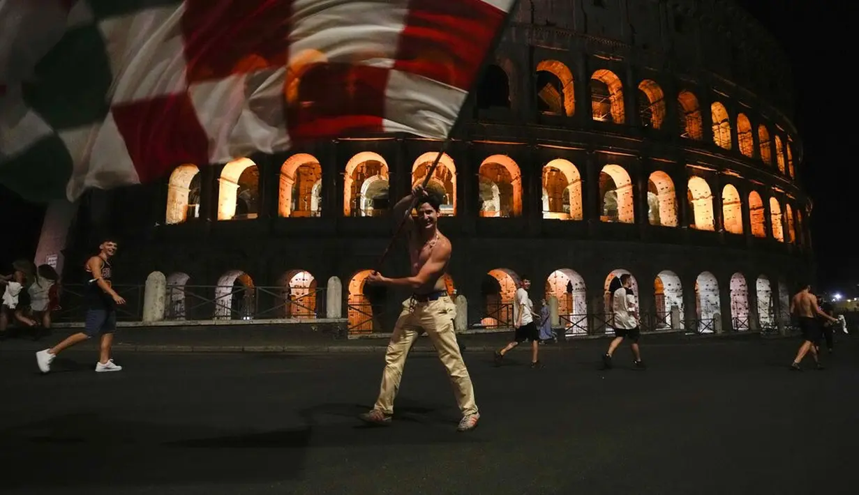 Suporter Italia mengibarkan bendara di depan Colosseum kuno Roma merayakan kemenangan atas Spanyol pada pertandingan semifinal Euro 2020, Roma, Rabu (7/7/2021). Gli Azzurri berhak ke final Piala Eropa 2020. (AP Photo/Alessandra Tarantino)
