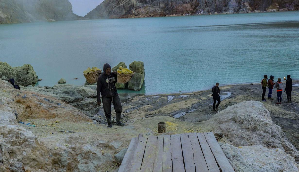 Danau kawah ini memiliki ukuran sekitar 960 x 600 meter dengan warna biru kehijauan. Meski tampak memesona, air danau tersebut memiliki tingkat keasaman yang sangat tinggi dan dikenal sebagai salah satu danau paling asam di dunia. Tampak dalam foto, penambang tradisional memikul bongkahan belerang dari dasar kawah Ijen di Banyuwangi, Jawa Timur. (merdeka.com/Arie Basuki)