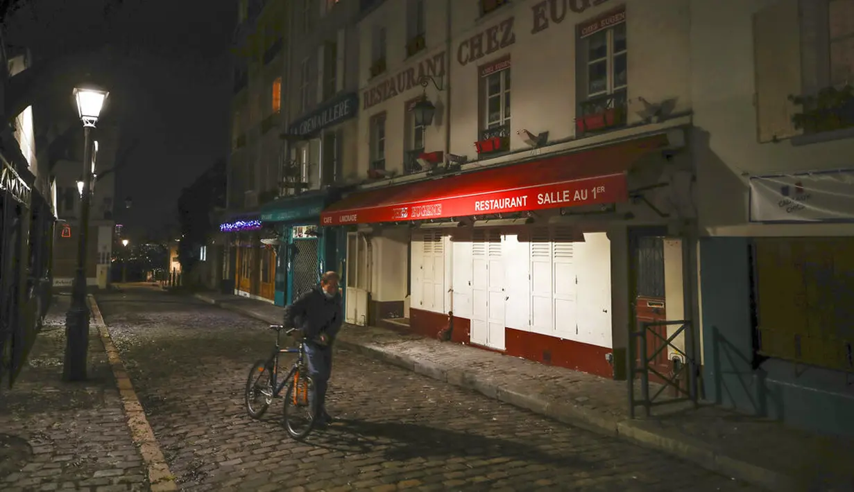 Seorang pria mendorong sepedanya di sepanjang deretan restoran yang tutup selama jam malam di Montmartre, Paris, Perancis, Selasa (15/12/2020). Pemerintah Perancis mencabut kebijakan lockdown terkait COVID-19 dan mulai memberlakukan jam malam. (AP Photo/Michel Euler)