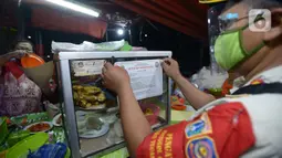 Petugas Satpol PP menempelkan stiker penutupan sementara tempat makan saat penertiban penerapan PSBB di wilayah Kecamatan Pulogadung, Jakarta, Jumat (18/9/2020). Malam, Razia dilakukan memastikan ketidakadaannya konsumen makan ditempat tersebut. (merdeka.com/Imam Buhori)