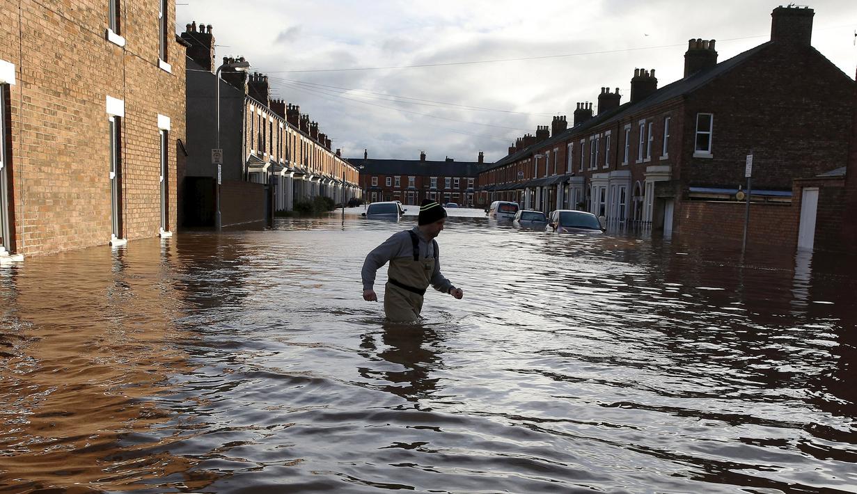 Seorang pria melintasi banjir yang merendam jalan pemukiman di Carlisle, Inggris, Minggu (6/12). Puluhan ribu rumah tidak punya listrik karena Badai Desmond yang menyebabkan banjir di Inggris utara dan sebagian Skotlandia. (REUTERS/Phil Noble)